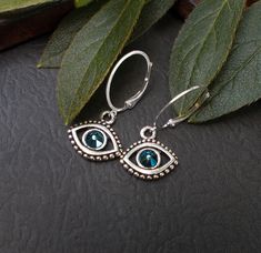 "Pretty blue crystal evil eye charms on modern oval ear wires. The charms are silver plated with an antiqued finish which highlights the flower pattern on the back. The modern ear wires are silver plated. These lightweight earrings are great for everyday wear and make a thoughtful gift idea, or an awesome treat for yourself.  Earring Length: about 1 1/4\" including the wire Charm Size: about 5/8\" wide Your earrings will arrive in an eco-friendly Kraft paper gift box with a ribbon. See What's New: https://www.etsy.com/shop/BonArtsStudio?ref=seller-platform-mcnav&section_id=23290134 My Shop Link: https://www.etsy.com/shop/BonArtsStudio Close-up photos showing item details may make an item appear larger - please check measurements and descriptions for actual size. Please contact me before pu Evil Eye Metal Jewelry For Gifts, Silver Round Evil Eye Earrings, Handmade Adjustable Eye-shaped Jewelry, Blue Evil Eye Dangle Jewelry, Crystal Blue Eyes, Wire Charm, Blue Sterling Silver Evil Eye Earrings, Luck Symbol, Symbol Jewelry