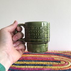 a hand holding a green coffee cup on top of a rug