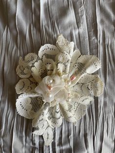 a white flower with pearls on it laying on a gray bed sheet and silver sheets