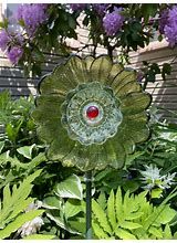 a green flower sitting in the middle of a garden filled with purple flowers and greenery