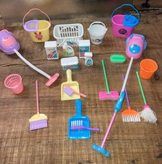 various toys and cleaning supplies laid out on a wooden surface, including brooms, mop, squirts, buckets, and other items