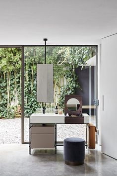 a bathroom with a sink, mirror and stool in front of a wall of plants