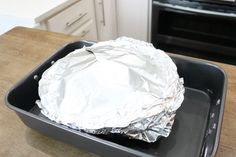 an aluminum foil covered dish sitting on top of a wooden table in front of an oven