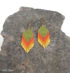 a pair of yellow and red beaded earrings sitting on top of a gray rock