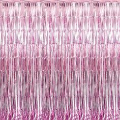 pink tinsel fringe curtain hanging from the ceiling in front of a white wall and window