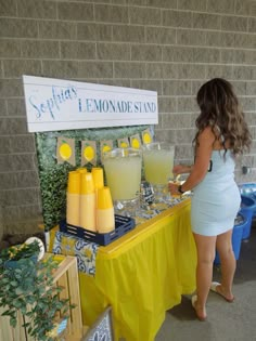 a woman standing next to a table filled with lemonades and glasses on it