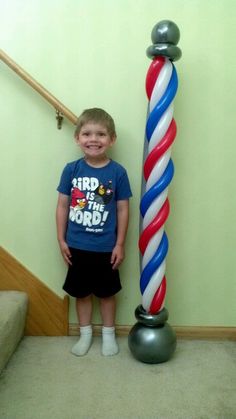 a young boy standing next to a tall red, white and blue object in front of a stair case