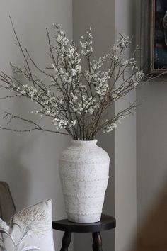 a white vase filled with flowers sitting on top of a table next to a pillow