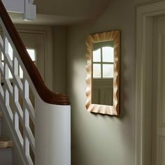 a mirror hanging on the wall next to a stair case in a room with white walls