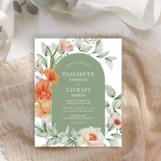 a wedding card with watercolor flowers and leaves on it, sitting on a blanket