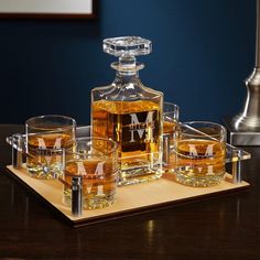 a wooden tray topped with glasses and a bottle of whiskey on top of a table