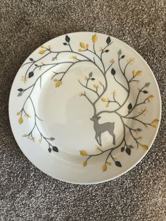 a white and yellow plate with a deer on it sitting on the floor next to a gray carpet