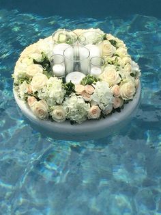 an arrangement of candles and flowers in the middle of a swimming pool with blue water