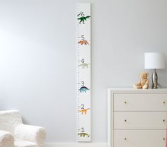 a child's growth chart with dinosaurs on it next to a white chair and lamp