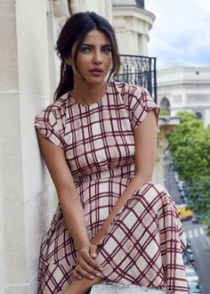 a woman sitting on the side of a building with her hand on her hip and looking at the camera