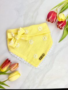 a yellow bandana with white flowers on it next to tulips and green leaves