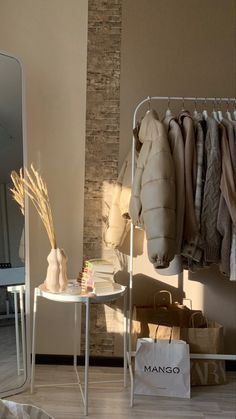 a white table and mirror in a room with clothes hanging on the rack next to it