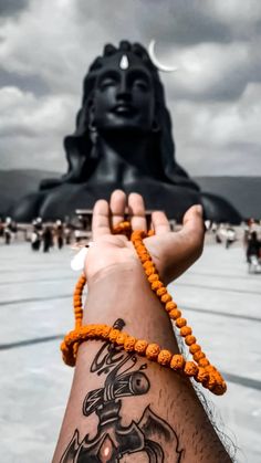 a person with a tattoo on their arm holding up a bracelet in front of a buddha statue