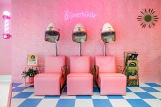 three pink chairs are in front of a wall with four lights on it, and there is a sign above them