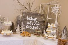 a table topped with cakes and cupcakes next to a sign that says baby it's cold outside