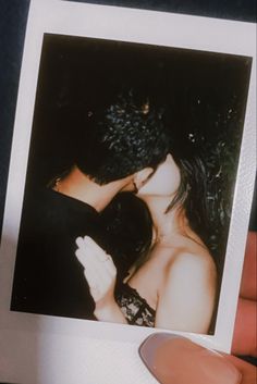 a hand holding a polaroid photo of a man kissing a woman