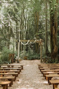 an outdoor ceremony set up in the woods with wooden benches and white draping