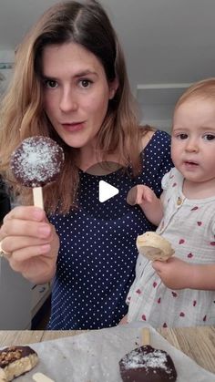 a woman holding a baby in her arms and eating desserts on a stick with chocolate