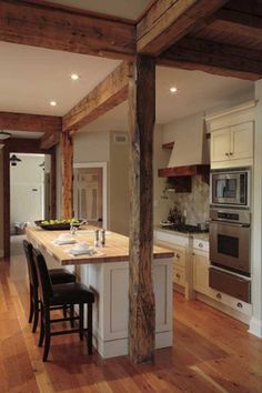 an open kitchen and dining room with wood flooring, white cabinets and wooden beams