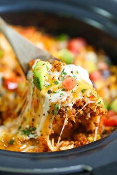 a crock pot filled with meat and vegetables covered in cheese, sauce, and sour cream