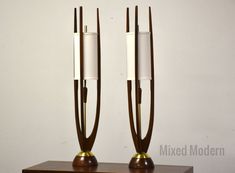 two lamps sitting on top of a wooden table next to each other in front of a white wall