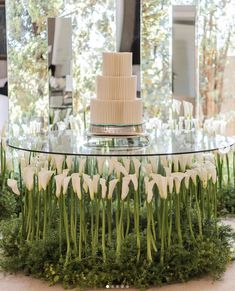 a cake sitting on top of a glass table next to flowers and greenery in front of a mirror