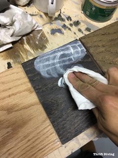 a person is painting on a piece of wood with white paint and black paper in front of them