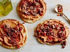 three pita breads with various toppings and a jar of olive oil on the side