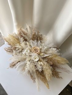 an arrangement of dried flowers and feathers on a white table cloth draped by a drape