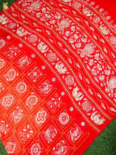 a red and white cloth with designs on it sitting on the ground next to grass