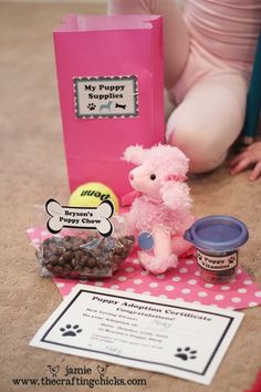 a pink teddy bear sitting on the floor next to a bag and some food items