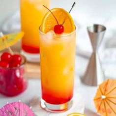 two glasses filled with orange juice and garnished with cherries next to umbrellas