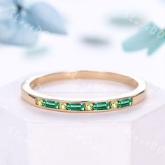 a gold ring with green stones on it and flowers in the background, sitting on a white surface