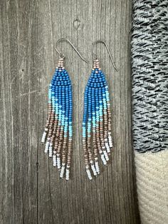 blue and brown seed beaded earrings on top of a wooden table next to a knitted blanket