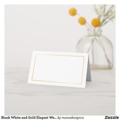 a white card with gold border sits next to a vase filled with yellow flowers