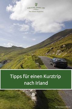 a car driving down a road next to a lush green hillside with water and mountains in the background