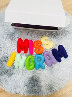 the word mom spelled out in multicolored letters on a furry surface next to a nintendo wii controller