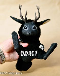 a hand holding a black stuffed animal with antlers on it's head that says custom