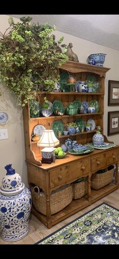 an old dresser with blue and white dishes on it's top, next to a potted plant