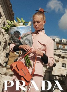 a woman holding a bag and flowers in front of a building with the words prada on it