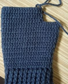 a blue crocheted dishcloth on a wooden table with a black object next to it