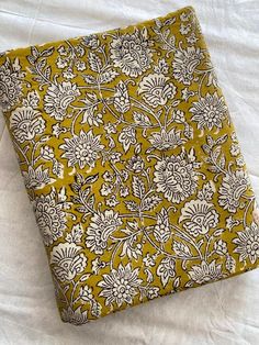 a yellow and white flowered cloth laying on top of a bed