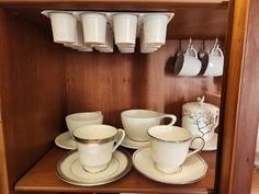 there are cups and saucers on the shelf next to each other in this cupboard