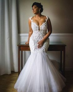 a woman in a white wedding dress standing next to a table with a window behind her