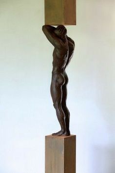 a bronze statue with a square shaped object on it's head and arms, standing in front of a white wall